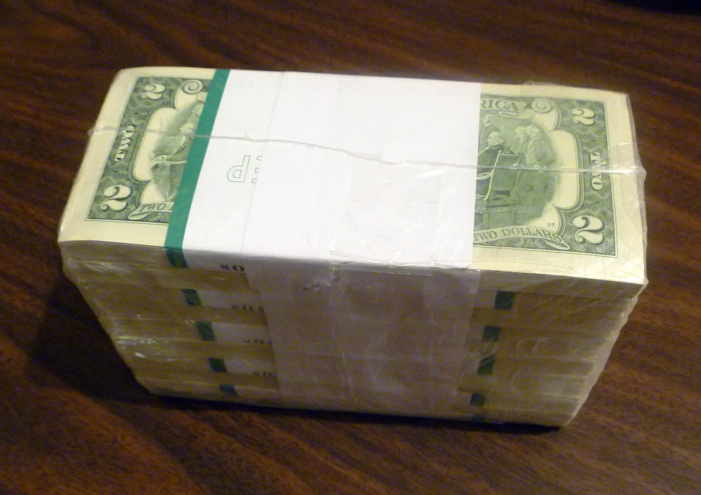 A shrink-wrapped bundle of United States two-dollar banknotes on a wooden surface