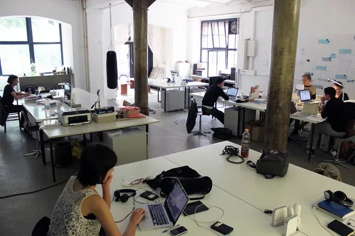 Menschen mit Laptops an mehreren Tischen in einem offenen Coworking-Büro in Berlin