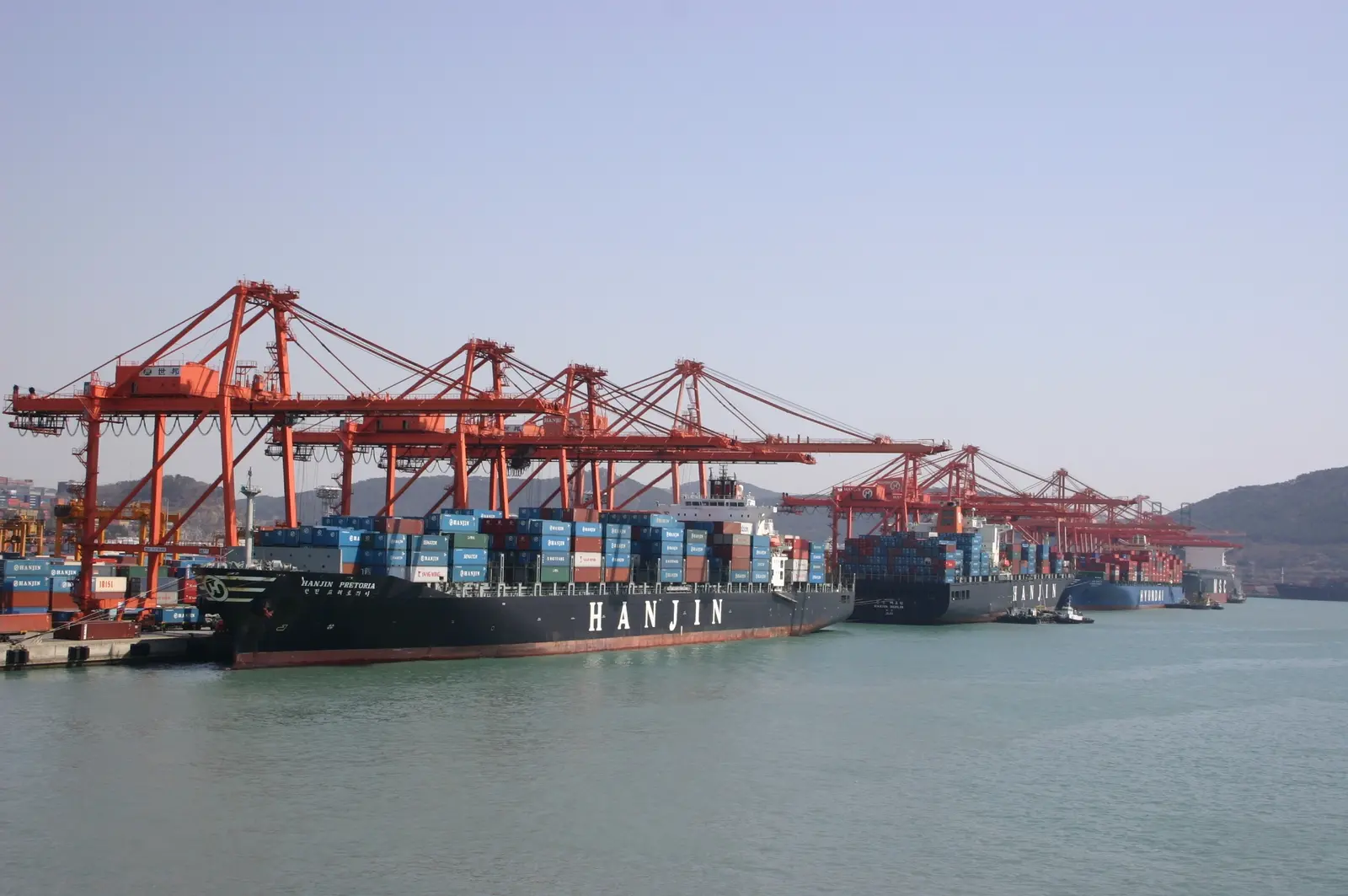 Container ship, red gantry cranes and stacked containers at Busan Container Terminal in South Korea.