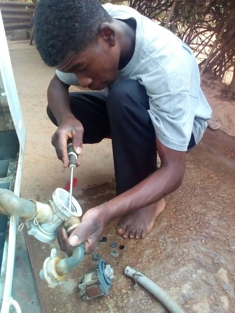 A person using a screwdriver to repair components of a twin-tub washing machine in Zambia