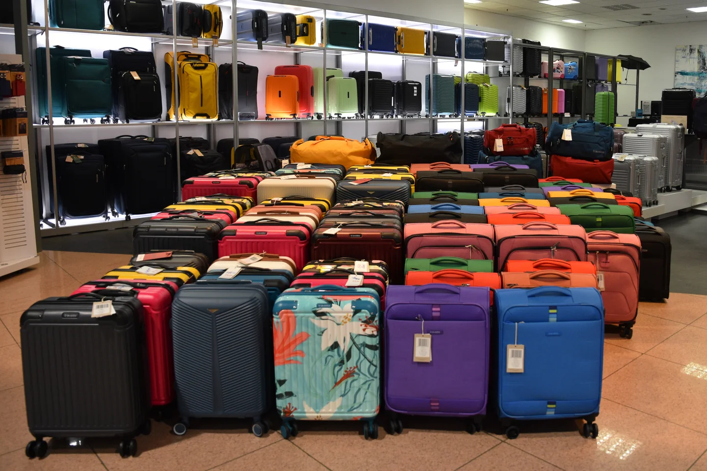 Rows of colorful wheeled suitcases displayed on the floor and shelves of a luggage store