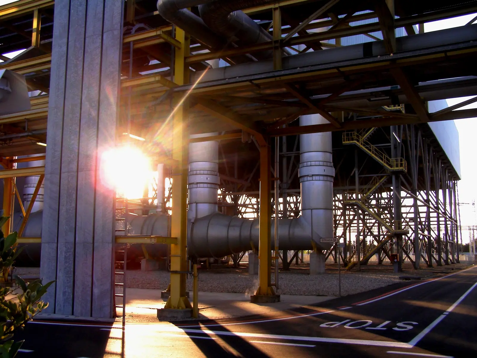 Metal structures and pipes at a natural gas power plant in Ferrera Erbognone, Italy, lit by the low sun.