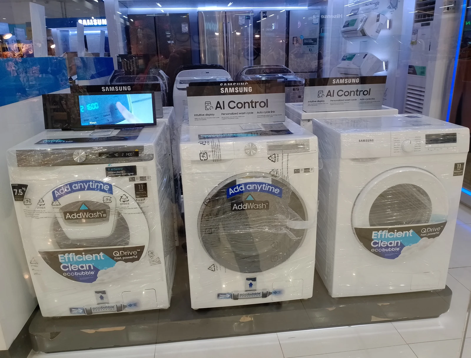 Several Samsung front-loading washing machines displayed behind a shop window at Parkmall.
