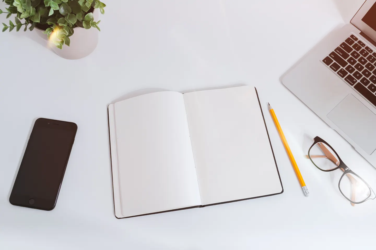 An open notebook, smartphone and laptop on a white desk